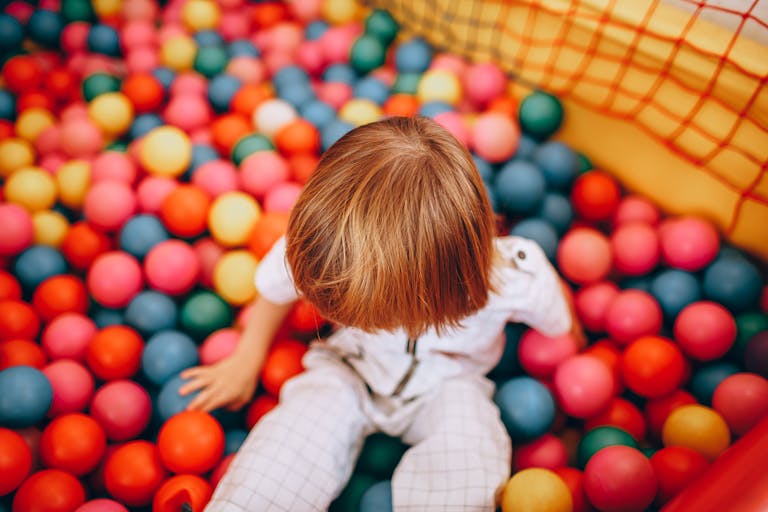 Top view of a child playing in a vibrant ball pit, enjoying a playful indoor activity.
