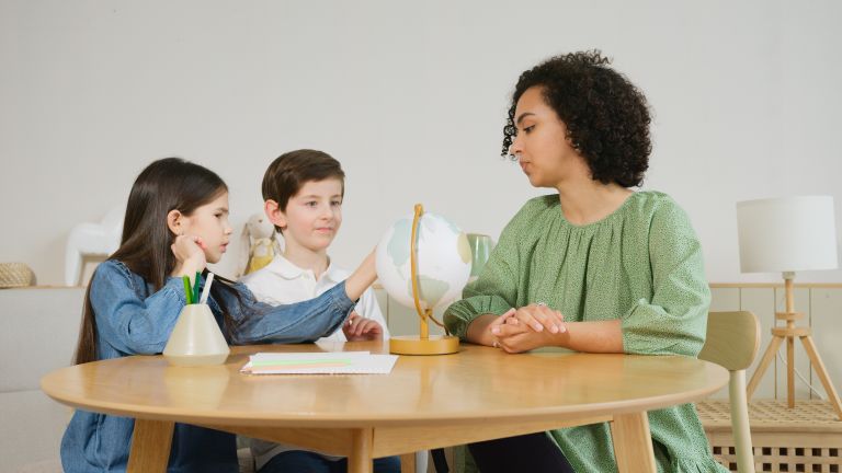 A teacher guides two children in a geography lesson using a globe.