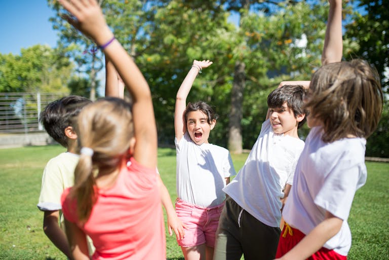 Group of children playing with raised arms in a sunny park, enjoying summer fun.