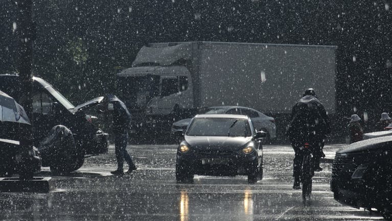 Moody urban street scene in heavy rain with cars and pedestrians.